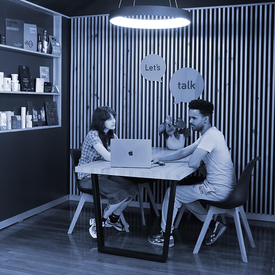 A woman and a man having a conversation at a table in a modern, stylish office space.