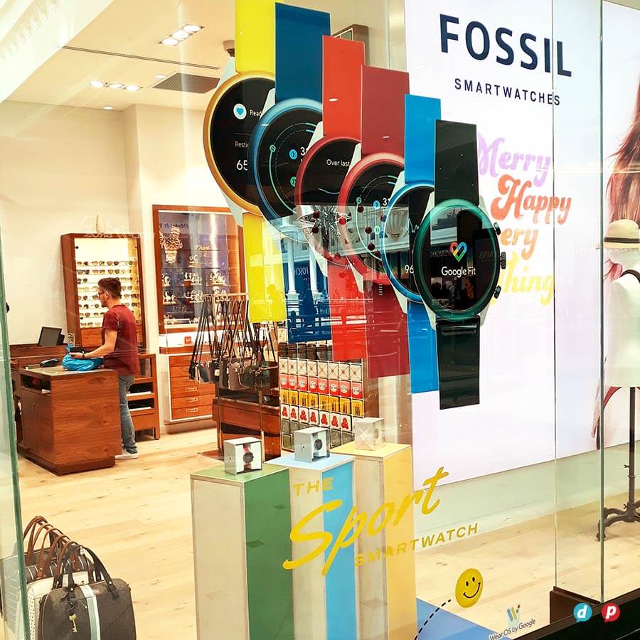 Fossil smartwatches display at a retail store with colorful stands and promotional signage.